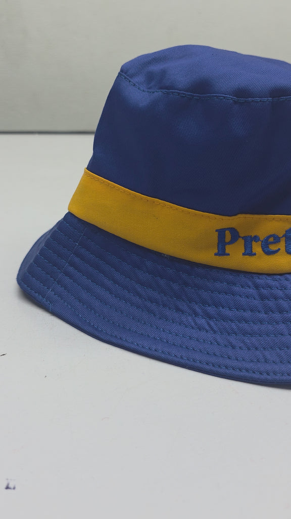 Blue bucket hat with gold band embroidered Pretty Poodle placed on white surface